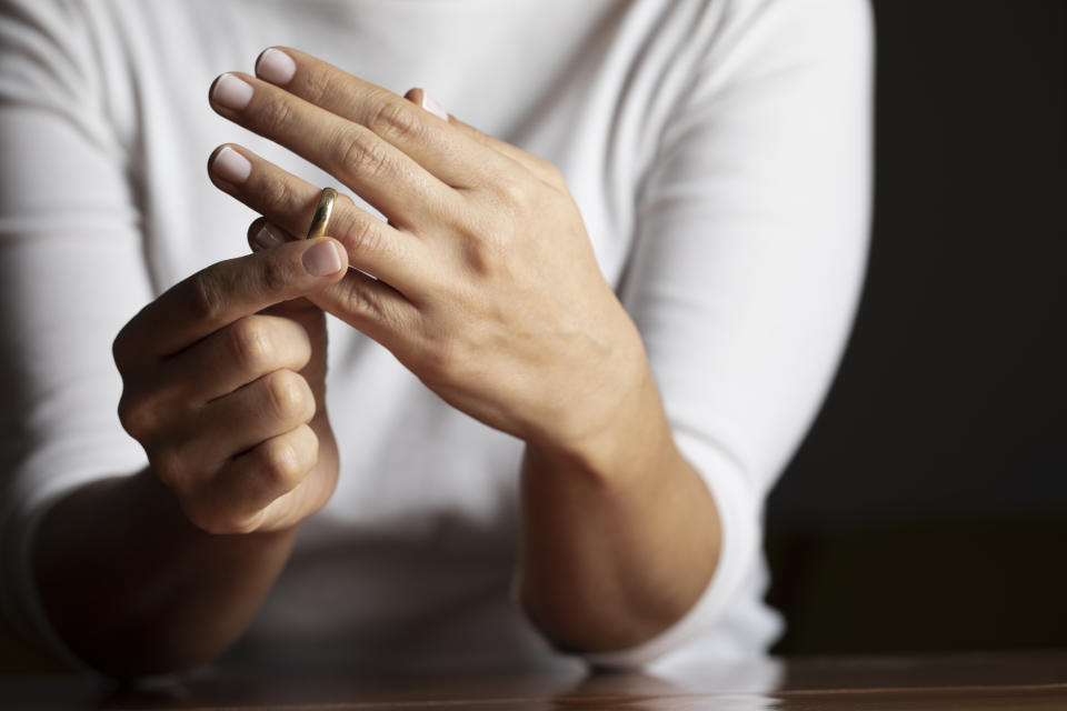 A person wearing a white long-sleeve shirt is seen removing a gold ring from their left ring finger