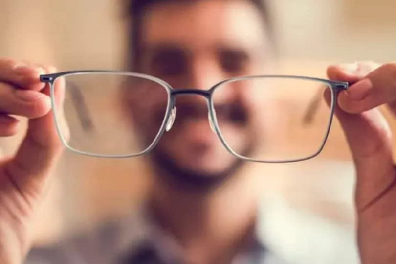An unidentifiable man is holding a pair of glasses to the camera lens.