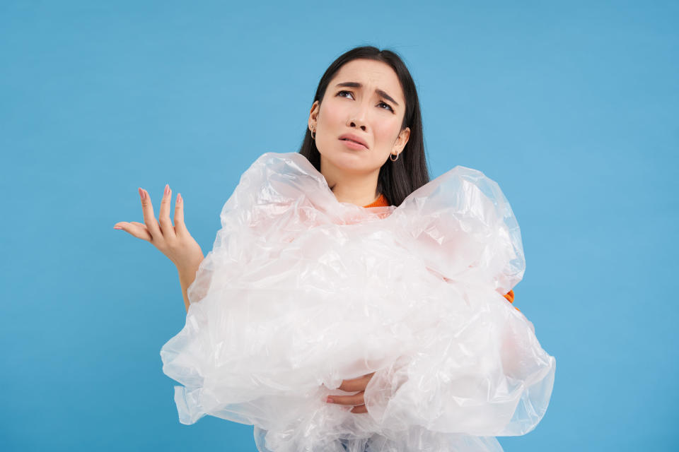 A woman holding a bunch of plastic, with her hand out and her face looking confused