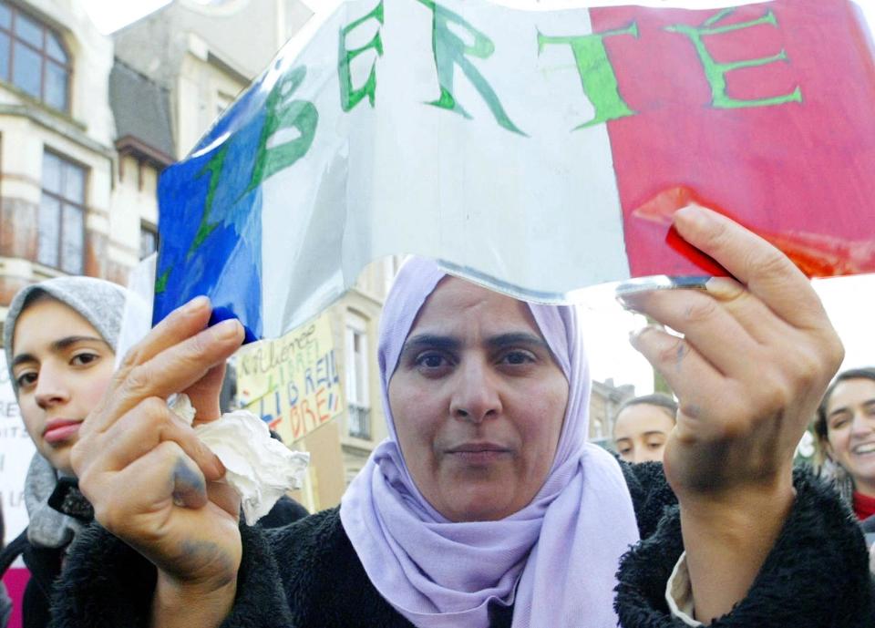 Woman holding a sign with 'LIBERTE' at a demonstration, surrounded by others