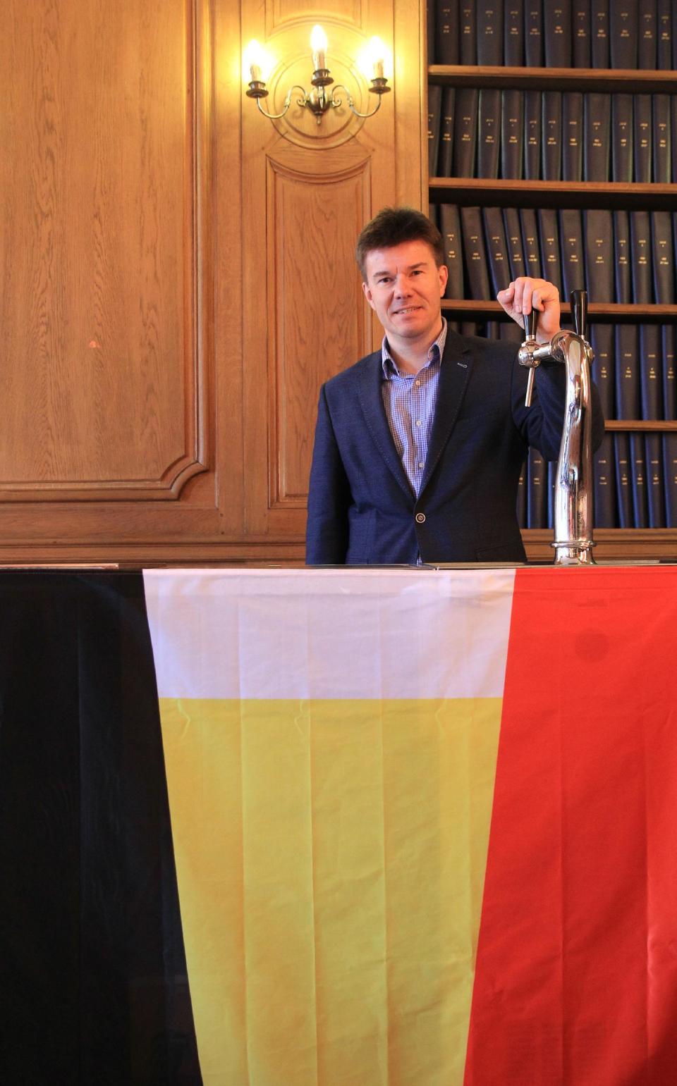 In this picture taken on Tuesday April 15, 2014, Sven Gatz, Head of the Belgian Brewers federation poses behind the Belgian tricolour, evoking a glass of beer, in Brussels. Thousands of bars in Belgian towns and villages have closed over the past decades, and on top of it, Belgians have stopped drinking like they used to. Now they have foreigners pick up the slack to keep the beer industry going. (AP Photo/Yves Logghe)