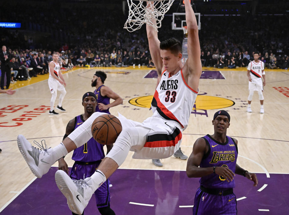 Portland Trail Blazers forward Zach Collins hangs from the rim after a dunk, as Los Angeles Lakers guards Kentavious Caldwell-Pope, left, and Rajon Rondo watch during the first half of an NBA basketball game Wednesday, Nov. 14, 2018, in Los Angeles. (AP Photo/Mark J. Terrill)