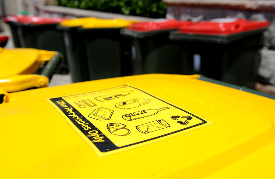 Recycling bins (yellow lids) sit with general waste bins on a nature strip in Sydney.