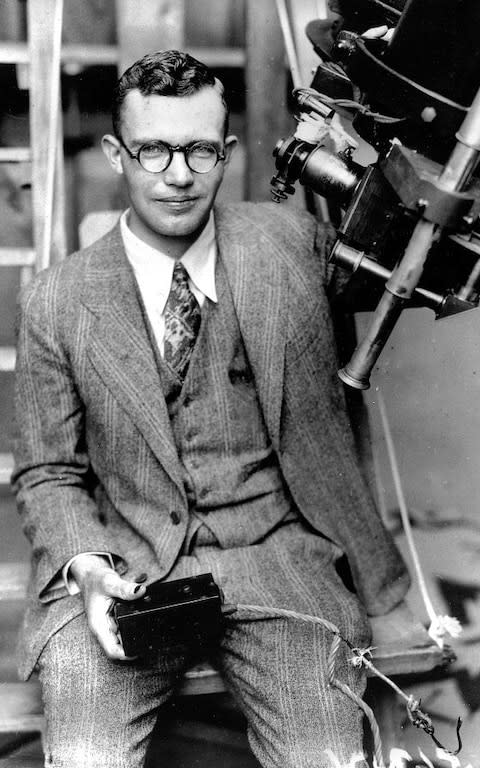 Clyde Tombaugh poses with the telescope through which he discovered the Pluto - Credit: Pluto Stowaway 