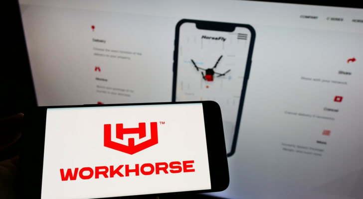 Person holding cellphone with logo of American electric vehicle company Workhorse Group Inc. (WKHS) on screen in front of webpage. Focus on phone display. Unmodified photo.