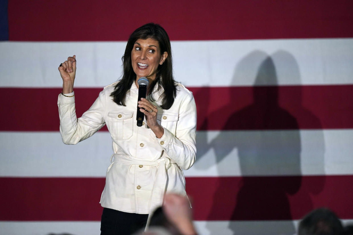 Republican presidential candidate Nikki Haley, in a white jacket, gestures with a huge American flag as a backdrop.