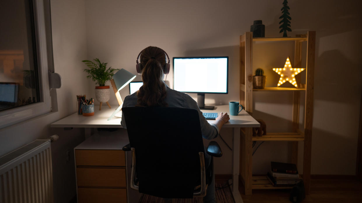 Rear view of an unrecognizable young woman working late on her computer from her home office.