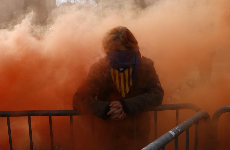 A pro-independence protestor stands surrounded by red smoke coming from a firemen protest in front of Catalonia's regional parliament as lawmakers voted inside, in Barcelona