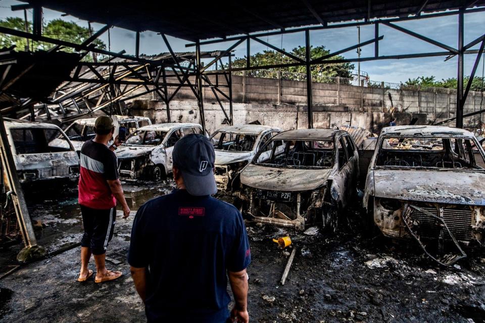 Two men look at burnt cars in Plumpang, north Jakarta on 4 March 2023, after a fire at a nearby state-run fuel storage depot run by energy firm Pertamina (AFP via Getty Images)