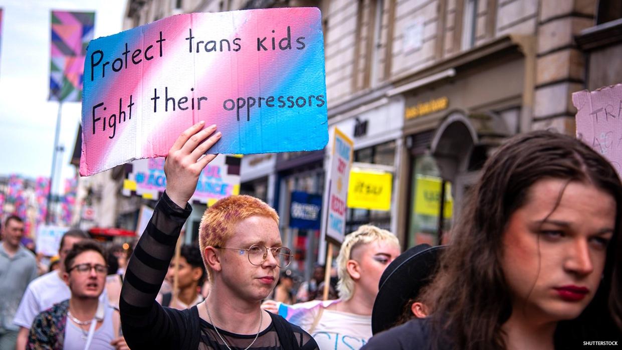 Protect Trans Kids banner being held by a person walking in a march.