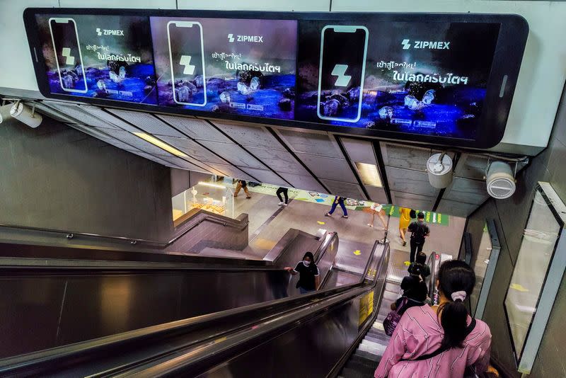 People walk past advertisement screen boards showing a crypto exchange platform "Zipmex" in Bangkok