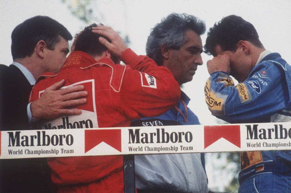 FILE - Italy's Nicola Larini, left, holds his head and Germany's Michael Schumacher, right, wipes a tear from his eyes while talking with Benetton director-general Flavio Briatore, center, on the podium following the San Marino Formula One Grand Prix crash in Imola, Italy, May 1, 1994. The drivers were reacting to the news that the Brazilian driver Ayrton Senna was in critical condition at a Bologna hospital after a crash in the race. Later it was announced that Senna had died after suffering severe head injuries. (AP-Photo/Claudio Luffoli, File)