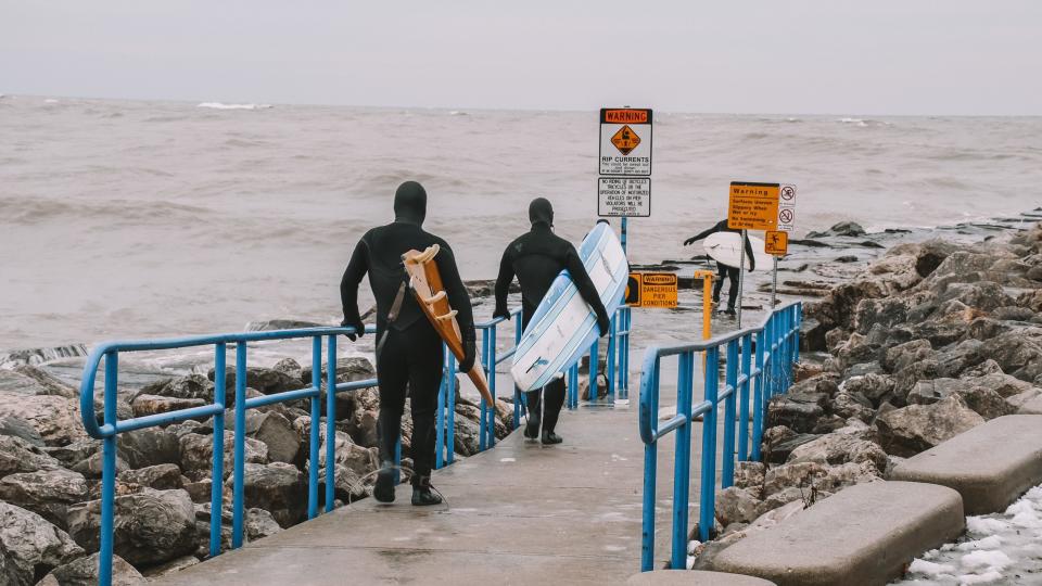 Surfers walk out to catch waves off of the Sheboygan pier.