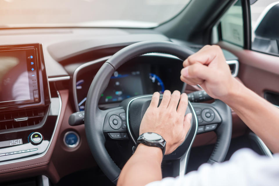 Person driving a car, hands on steering wheel, dashboard and infotainment system visible