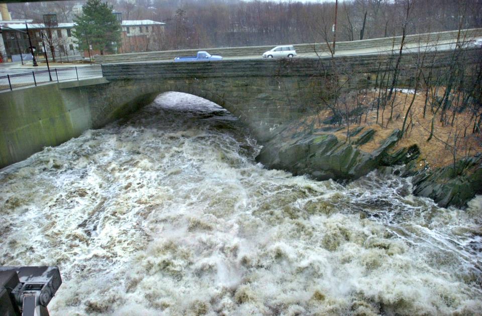 The Blackstone River, swollen by heavy rain in 2001, rushes over the Thundermist Dam and under the South Main Street bridge in Woonsocket.