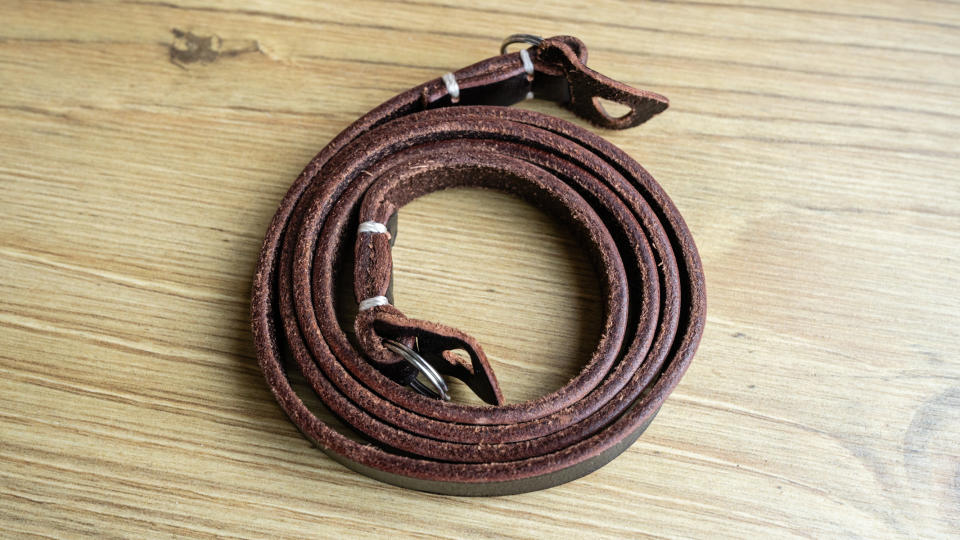 Thin brown leather camera strap rolled up on a wooden floor