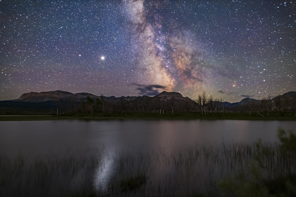 The galactic core area of the Milky Way over Maskinonge Pond in Waterton Lakes National Park, Alberta. Jupiter is the bright object at left, with Saturn dimmer to the left (east) of Jupiter. In the summer of 2020 the two planets were close together in the summer sky. Jupiter provides the glitter path on the water. Antares and Scorpius are to the right. Sagittarius is at centre. This was July 13-14, 2020. As is typical of Waterton, it was windy enough tonight that there was no sharp reflection of the stars and Milky Way in the water. This is a stack of 12 exposures for the ground, mean combined to smooth noise in the dark foreground, with the sky from one exposure, all untracked for 30 seconds at f/2 with the Sigma 20mm lens on the Canon EOS Ra camera at ISO 3200. Stacked and blended in Photoshop. (Photo by: Alan Dyer/VW PICS/Universal Images Group via Getty Images)