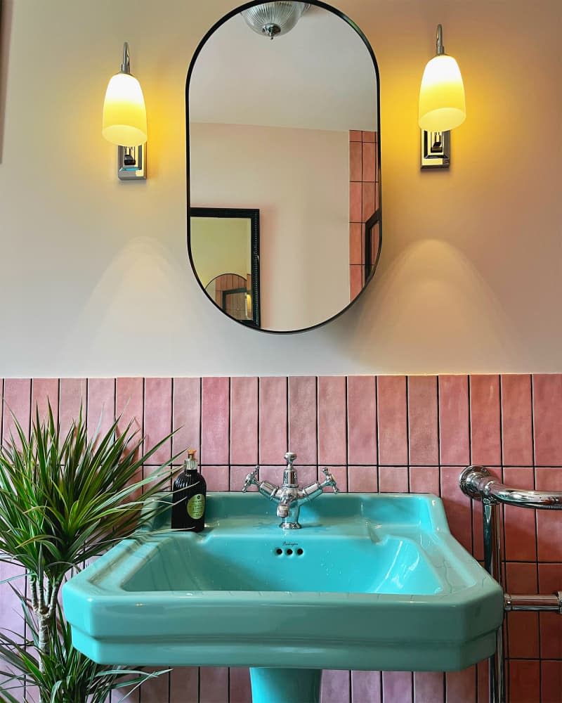 Turquoise pedestal sink in bathroom with pink wainscoting and pill shaped mirror.