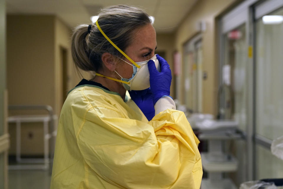 FILE - In this Nov. 24, 2020, file photo, registered nurse Chrissie Burkhiser puts on personal protective equipment as she prepares to treat a COVID-19 patient in the in the emergency room at Scotland County Hospital in Memphis, Mo. The U.S. has seen a dramatic turnaround since December and January, when hospitals were teeming with patients after holiday gatherings and pandemic fatigue caused a surge in cases and deaths. (AP Photo/Jeff Roberson, File)