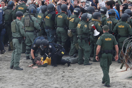 Police officers detain a man during a gathering in support of the migrant caravan in San Diego, U.S., close to the border wall between the United States and Mexico, as seen from Tijuana, Mexico December 10, 2018. REUTERS/Carlos Garcia Rawlins