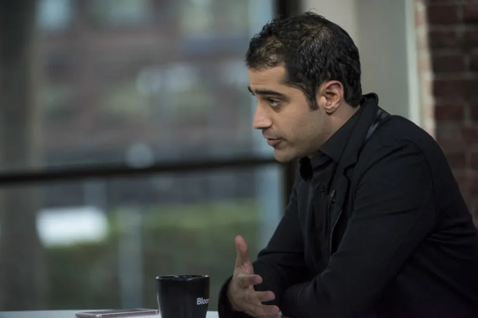 Kayvon Beykpour is seen speaking to a reporter (who is off-screen) during an interview with Bloomberg. Beykpour&#39;s phone and a cup of coffee lay on the table in front of him.