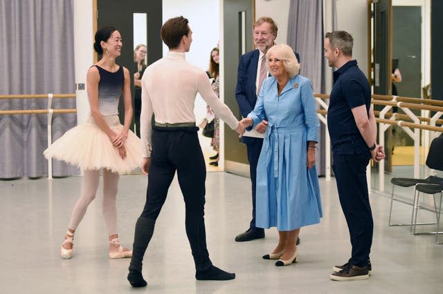 The Queen, in a blue dress, shakes hands with a male ballet dancer