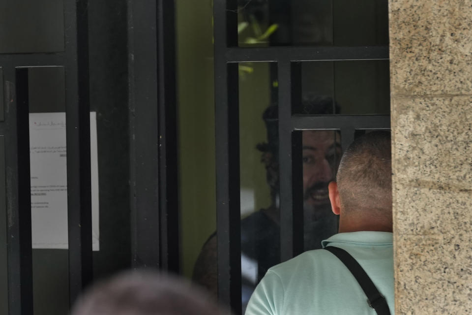 An armed man Bassam al-Sheikh Hussein, 42, background, speaks with a security officer after he took hostages inside a bank, in Beirut, Lebanon, Thursday, Aug. 11, 2022. A hostage standoff in which a gunman demanded a Beirut bank let him withdraw his trapped savings so that he could pay his father's medical bills ended seven hours later with the man's surrender Thursday. (AP Photo/Hussein Malla)