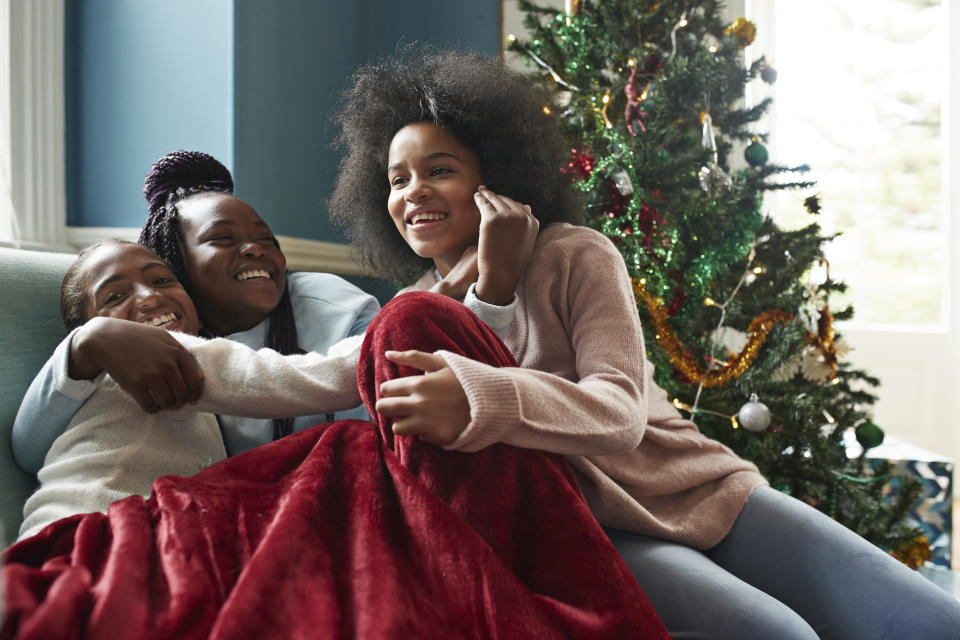Happy sisters embracing while sitting on sofa by Christmas tree at home