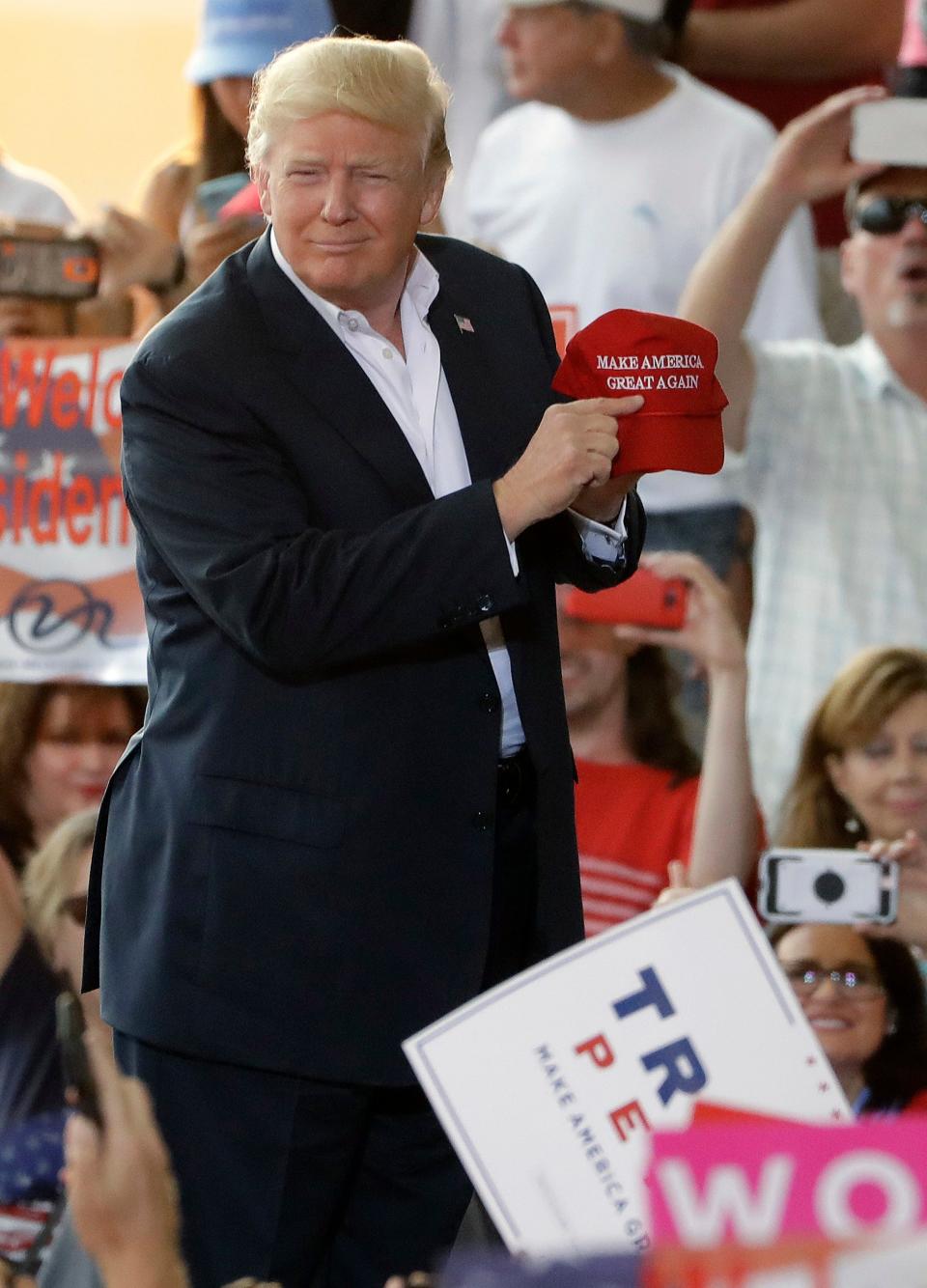 President Donald Trump points to a slogan on a hat during the "Make America Great Again Rally" at Orlando-Melbourne International Airport Saturday, Feb. 18, 2017, in Melbourne, Fla