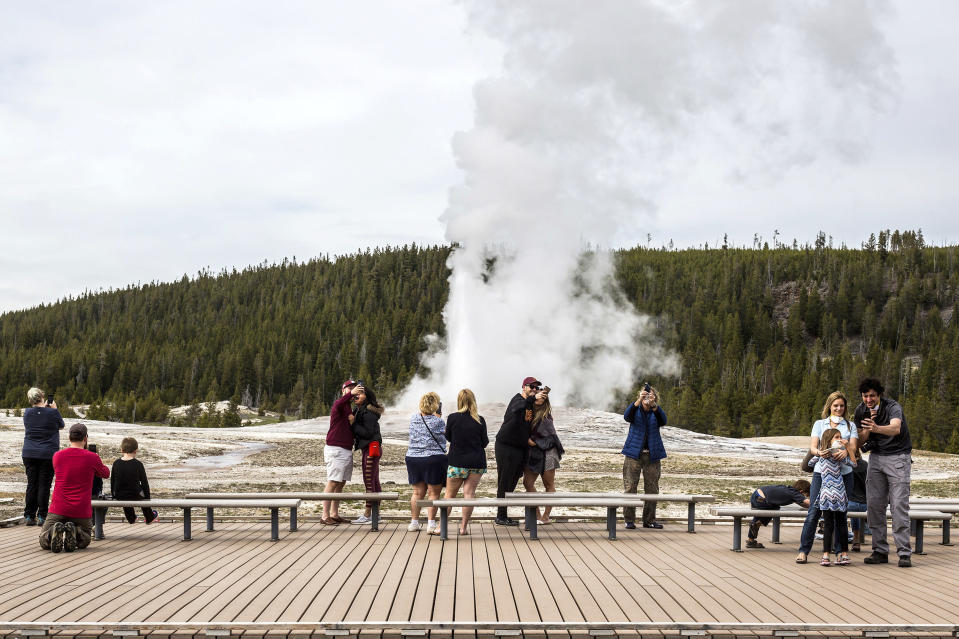 FILE - In this May 18, 2020, file photo, visitors watch as Old Faithful erupts at Yellowstone National Park, Wyo. Americans may soon get a better glimpse into a future of green-friendly transportation by visiting a U.S. national park. It’s a joint pledge being signed Wednesday by Interior Secretary Deb Haaland and Transportation Secretary Pete Buttigieg to test some of the newest and most innovative travel technologies on public lands. The plan is being made possible by the $1 trillion infrastructure law and other federal spending. Under new pilot programs, visitors to national parks could see self-driving shuttle buses, along with more electric scooter or bike stations and electric charging stations for travelers in zero-emission cars. Yellowstone National Park would see some of the most immediate updates, with other sites to follow. (Ryan Dorgan/Jackson Hole News & Guide via AP, File)