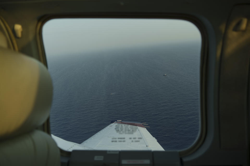 A small migrant boat, left, and a Libyan merchant vessel are visible through the window of the humanitarian aircraft Seabird, above the Mediterranean Sea between Libya and Italy, Tuesday, Oct. 5, 2021. The unseaworthy boat was spotted by the Seabird, a monitoring aircraft operated by the Sea-Watch non-governmental organization that seeks to monitor human rights violations and assist in the rescue of migrants fleeing Libya to Europe by boat on the Mediterranean Sea. (AP Photo/Renata Brito)