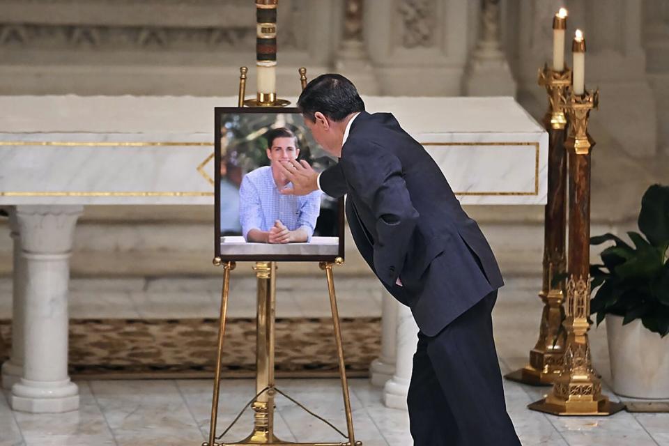 A man, wearing a dark suit, stands facing away and toward a photo in a black frame sitting on display in a church