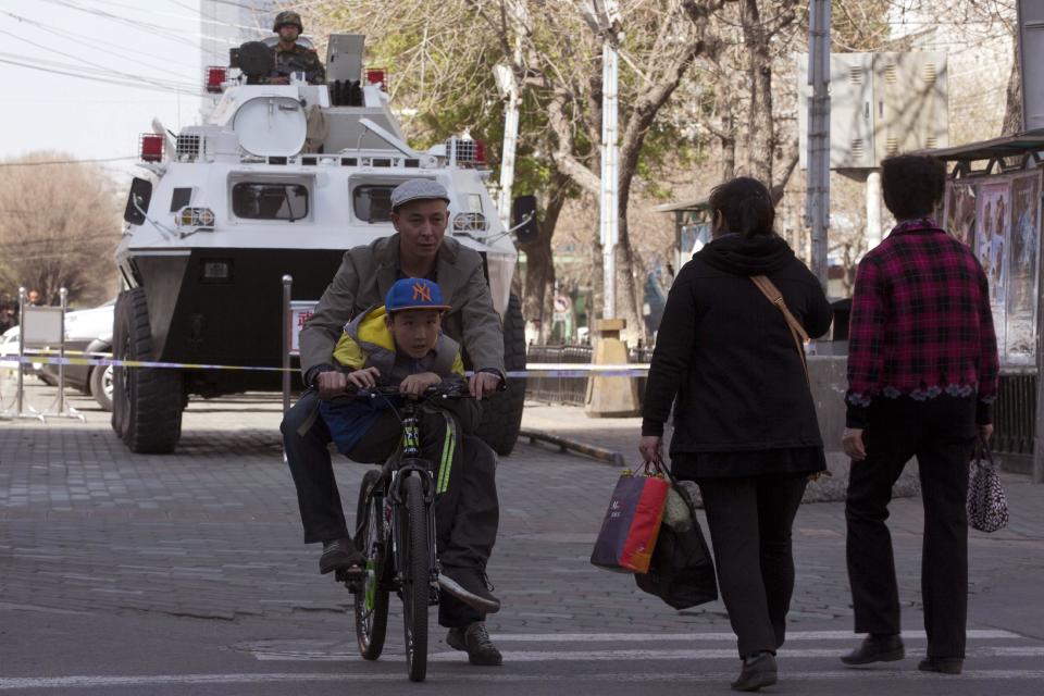 A man and child on a bicycle cycle past by an armored paramilitary police vehicle parked outside a hospital where victims of Wednesday's explosion receives treatment in Urumqi in northwest China's Xinjiang Uygur Autonomous Region on Thursday, May 1, 2014. Chinese President Xi Jinping has demanded "decisive actions" against terrorism following an attack at a railway station in the far-west minority region of Xinjiang that left three people dead and 79 injured. (AP Photo/Ng Han Guan)