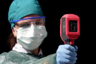 A healthcare worker measures body temperature as a precaution against the spread of the new coronavirus in COVID-19 hospital in Sarajevo, Bosnia, Monday, July 27, 2020. Regional WHO office in Bosnia expressed its concern with recent reports that medical institutions around the country are closing to maximum capacity as recent spike in COVID-19 infections are reaching record levels. (AP Photo/Eldar Emric)