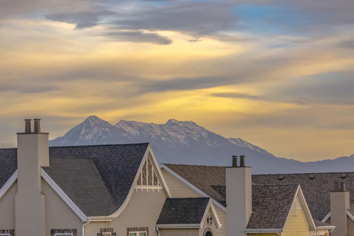 Roof of homes against mountain and sky in Utah. View of the roofs of homes with chimneys in Daybreak Utah community. The majestic Wasatch mountains and glowing cloudy sky can be seen in the bckground.