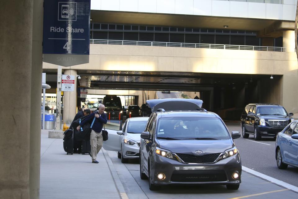 Passengers find their rides at the Ride Share point as they exit Phoenix Sky Harbor International Airport Wednesday, Dec. 18, 2019, in Phoenix. The Phoenix City Council is set to vote on raising fees charged to ride-hailing companies at the airport. If approved Wednesday afternoon, the proposal will increase the current fee from $2.66 per pickup. That would jump to $4 starting Jan. 1 and be applied to drop-offs as well. (AP Photo/Ross D. Franklin)