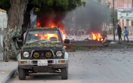 An abandoned car is seen near the wreckage of a burning vehicle at the scene of an attack where a car laden with explosives rammed into a cafeteria in Somalia's capital Mogadishu, May 8, 2017. REUTERS/Feisal Omar