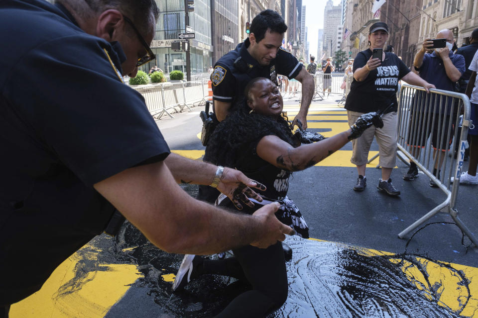 NYPD officers attempt to detain a protester who poured black paint on the Black Lives Matter mural outside of Trump Tower on Fifth Avenue in the Manhattan borough of New York on Saturday, July 18, 2020. (AP Photo/Yuki Iwamura)