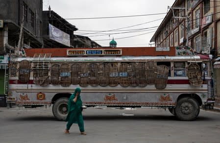 FILE PHOTO: A Kashmiri woman walks past a bus used as a road block by Indian security personnel during restrictions after the scrapping of the special constitutional status for Kashmir by the government, in Srinagar