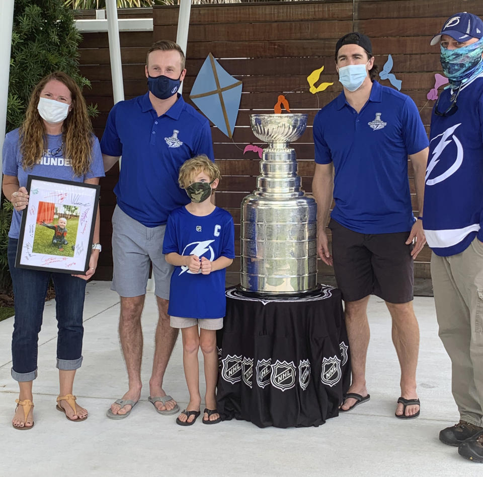 Christen, left, and Jim Gray, right, and son Declan , third from left, pose with the Stanley Cup with Tampa Bay Lightning players Steven Stamkos, second from left, and Ryan McDonagh, second from right, at the Children’s Cancer Center in Tampa, Fla., on Oct. 16, 2020. Christen holds a framed picture of her youngest son, Finn, who died from Ewing’s Sarcoma in January. The Lightning took the Stanley Cup to the Children’s Cancer Center as part of their local tour of stops after winning the National Hockey League’s championship trophy Sept. 28 in Edmonton, Alberta. ( Kristina Hjertkvist/Tampa Bay Lightning via AP)