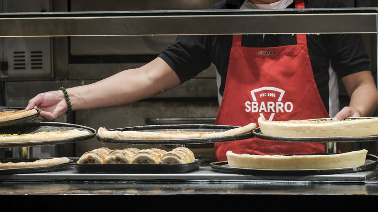 Sbarro worker putting pizzas on display 