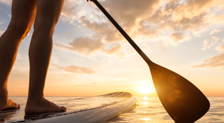 Stand up paddle boarding on a quiet sea with warm summer sunset colors, close-up of legs