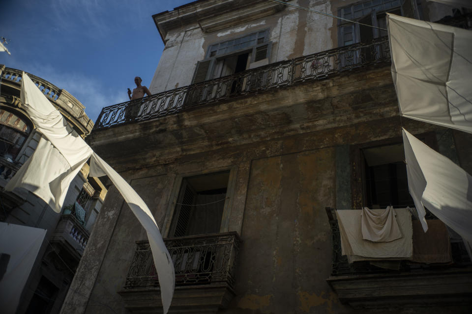 In this Nov. 9, 2019 photo, a man stands on the balcony of his home amid drying sheets in Havana, Cuba. The city of Havana will celebrate its 500th anniversary on Nov. 16. (AP Photo/Ramon Espinosa)