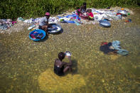 Geraldine Pierre 14, front, eats as she takes a break from washing clothes with her family in the Meille River near a former UN base in Mirebalais, Haiti, Monday, Oct. 19, 2020. Ten years after a cholera epidemic swept through Haiti and killed thousands, families of victims still struggle financially and await compensation from the United Nations as many continue to drink from and bathe in a river that became ground zero for the waterborne disease. (AP Photo/Dieu Nalio Chery)