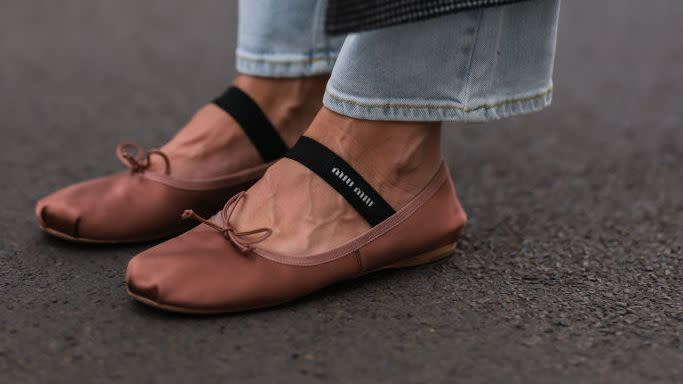 a woman on the street in berlin wearing dark pink satin ballet flats by miu miu with jeans and coat in a roundup of the best satin ballet flats 2024