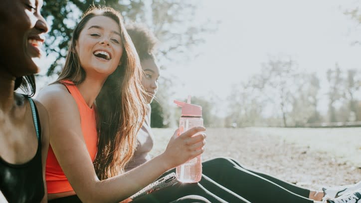  A woman wearing fitness clothing, sat in a park with friends while holding a reusable water bottle 