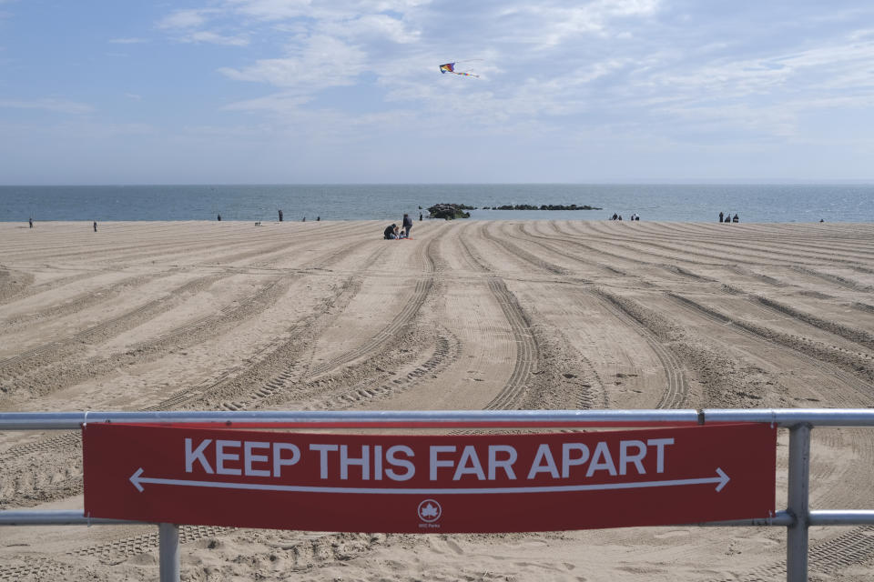 FILE - In this April 12, 2020, file photo, a sign on the Coney Island boardwalk reminds people to keep their distance in New York. From Cape Cod to California, festivals are being canceled, businesses in tourist havens are looking at empty reservation books, and people who have been cooped up through a dismal spring are worrying summer will bring just more of the same. (AP Photo/Seth Wenig, File)