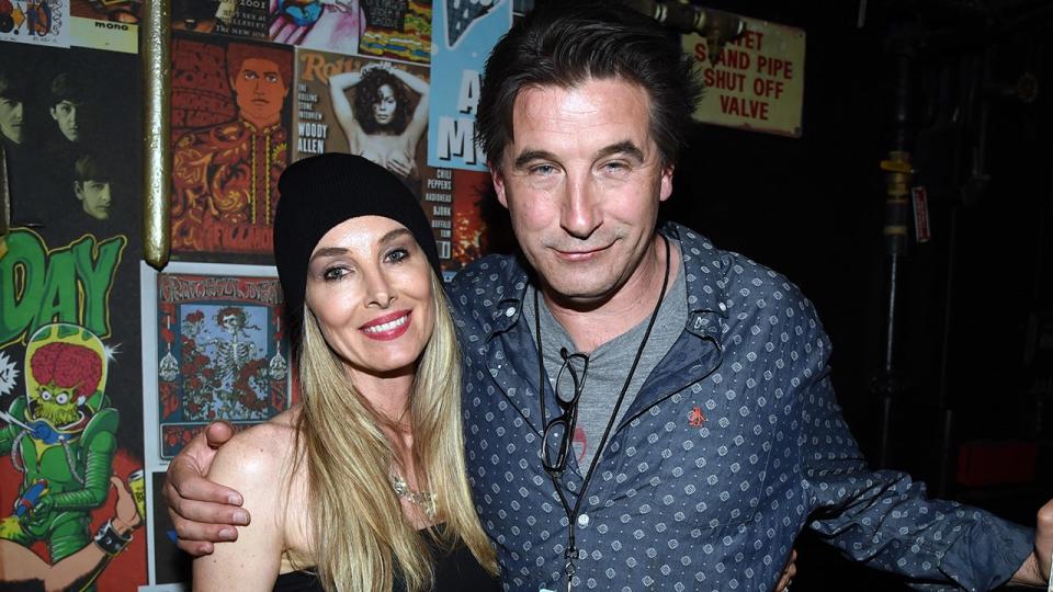 Chynna Phillips wearing a black beanie smiles next to husband Billy Baldwin in a blue patterned shirt