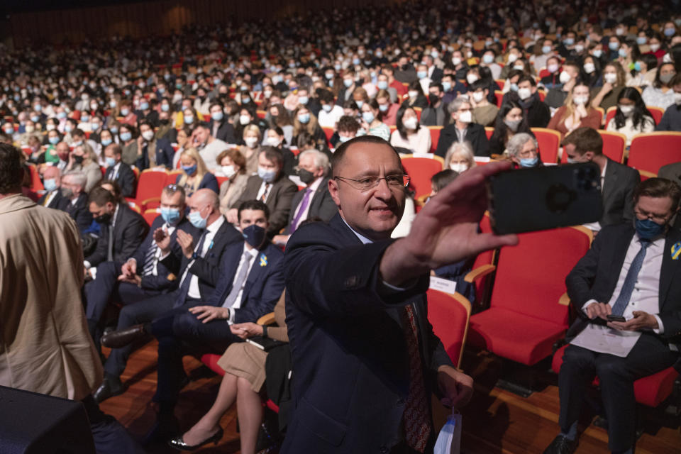 In this photo provided by the Australian National University Ukrainian Ambassador to Australia Vasyl Myroshnychenko takes a selfie with the crowd before Ukrainian President Volodymyr Zelenskyy appears on a screen during his online address to the university in Canberra, Australia, Wednesday, Aug. 3, 2022. Zelenskyy is addressing 21 Australian universities in an online discussion hosted by the Australian National University. (Tracey Nearmy/ANU via AP)