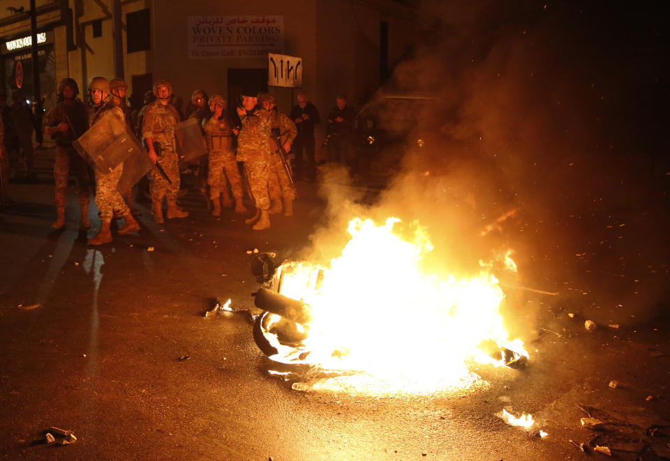 Lebanese army soldiers stand near a motorcycle that was set on fire by protesters, during a clash between supporters of the Shiite Hezbollah and Amal groups and the anti-government protesters, in Beirut, Lebanon, early Monday, Nov. 25, 2019. Security forces fired tear gas amid confrontations in central Beirut that went into Monday morning between Hezbollah supporters and demonstrators protesting against Lebanon's political elite. (AP Photo/Hussein Malla)